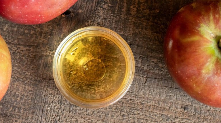 Jar of apple cider vinegar is kept on a wooden table along with apples