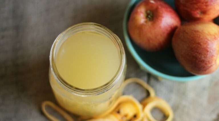 Jar of apple cider vinegar with honey is kept on wooden table along with bowel of apple