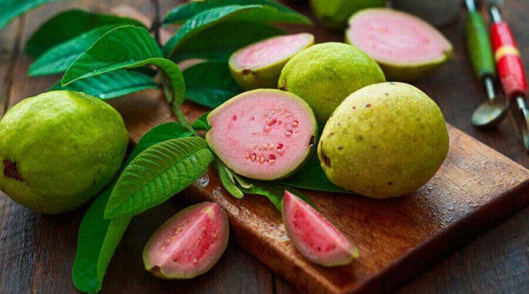 The chopped and whole guava is placed on wooden board along with guava leaves