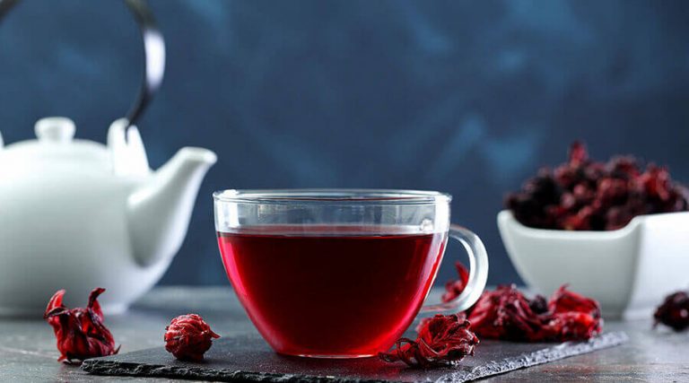 A cup of hibiscus tea along with pot and dry leaf were placed on a wooden table