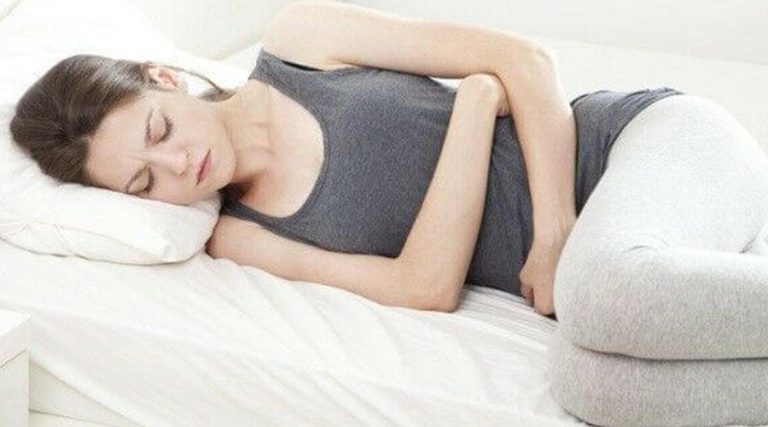 A woman lying on her side in discomfort, holding her stomach, conveying a sense of pain or unease