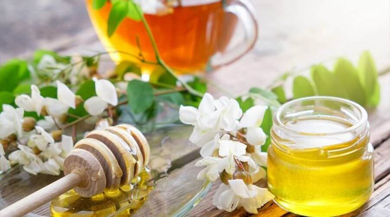 a cup of white acacia tea was placed on the wooden table along with its leaves