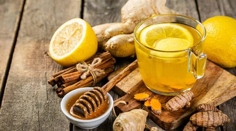 a glass of ginger honey tea next to bowl of honey and lemons