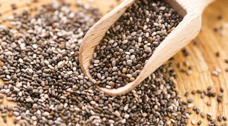 A wooden scoop and chia seeds are placed on a wooden table.