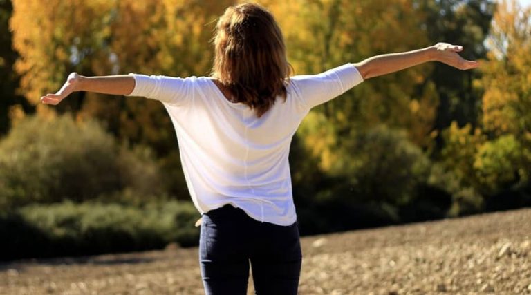 A woman is stretching with her arms spread wide.