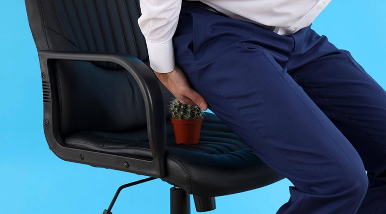 A man sitting on a chair with a cactus beneath him, symbolizing discomfort or pain, often associated with conditions like hemorrhoids.