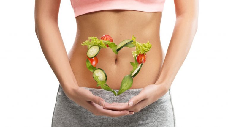 A woman's abdomen highlighted by a heart shape made of fresh vegetables, symbolizing the connection between a balanced diet and gut health.