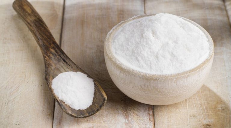 a bowl and spoon filled with baking soda placed on a wooden table