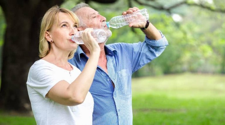 couple drinking water from a bottle in a park