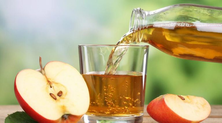 pouring apple cider vinegar in a glass from a jar next to sliced apple