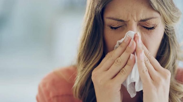 blonde women with sinusitis wiping her nose with a tissue