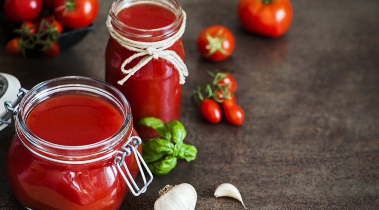 Two glass jars filled with vibrant red homemade tomato sauce are displayed on a rustic kitchen countertop