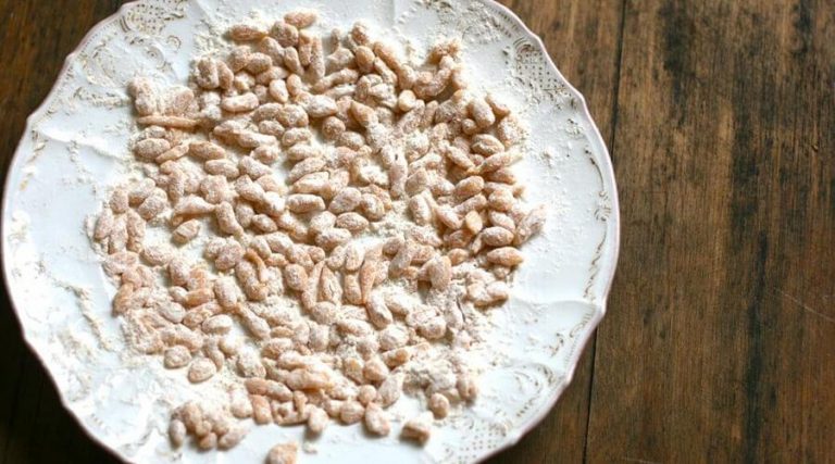 A plate filled with small, bite-sized pieces of a sweet treat, dusted with powdered sugar, placed on a wooden table