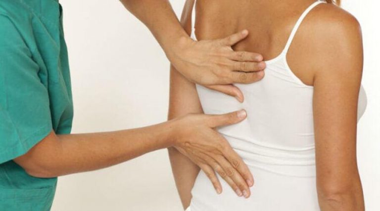 A physical therapist carefully examines a patient's back, assessing alignment and providing hands-on treatment