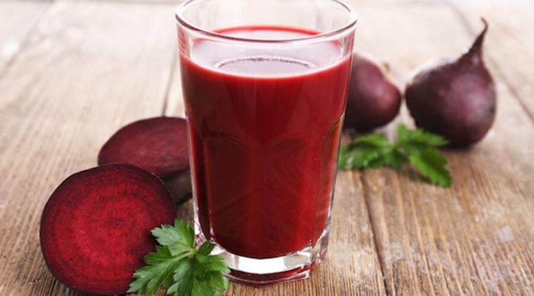a glass of beetroot juice next to sliced beetroot placed on a wooden table