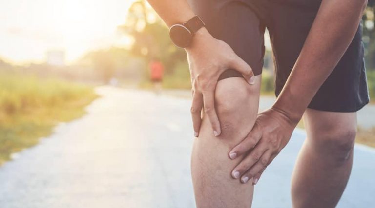 man standing on street while holding his knee because of limb pain