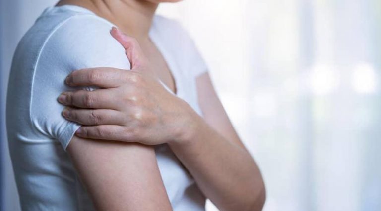 a woman in white t-shirt holding her shoulder in pain