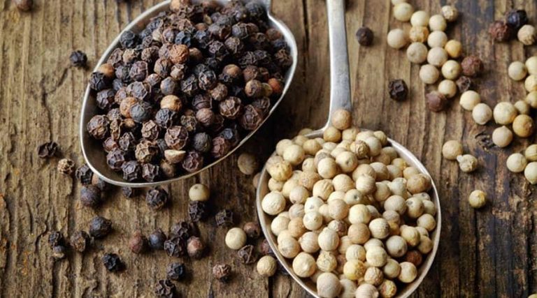 bowls of black pepper and white pepper placed on a wooden table