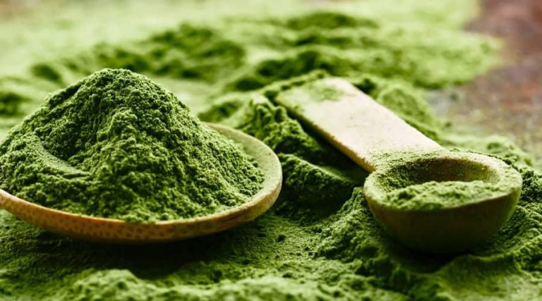 green barley powder spilled on a wooden table with a wooden teaspoon