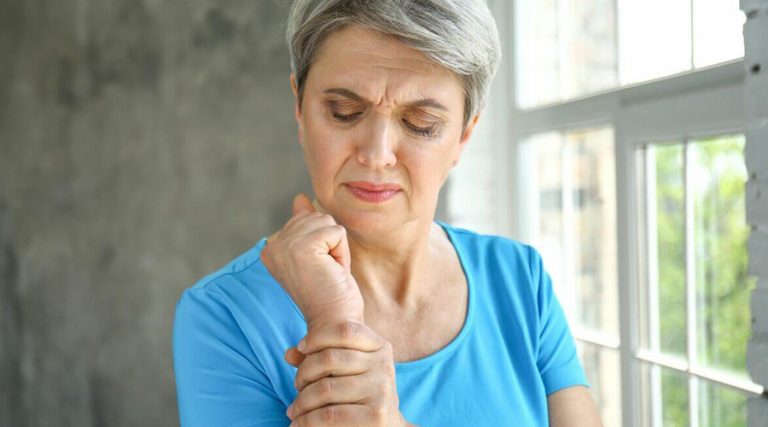 old women having joint pain holding her arm with blur background
