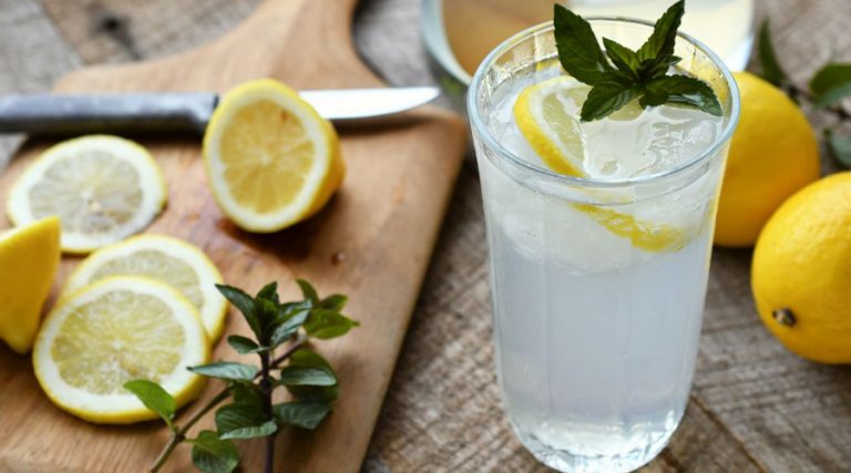 a glass of lemon water surrounded by lemons and mint