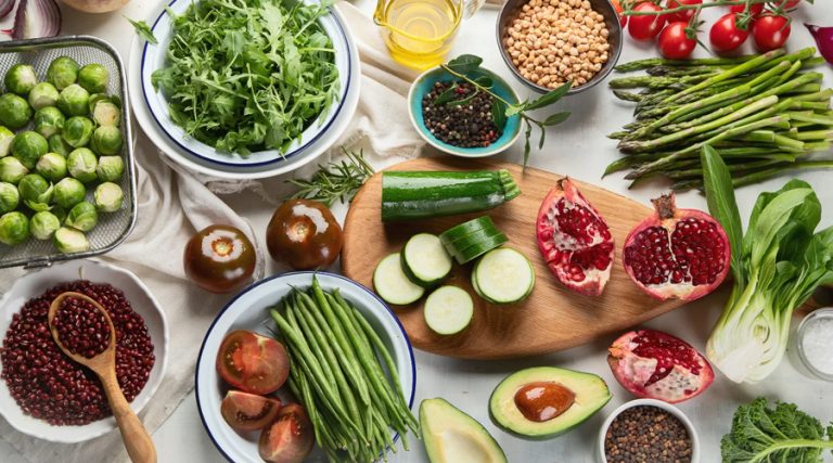 A colorful flat lay of fresh plant-based ingredients arranged on a white surface, showcasing a variety of vegetables, fruits, and legumes