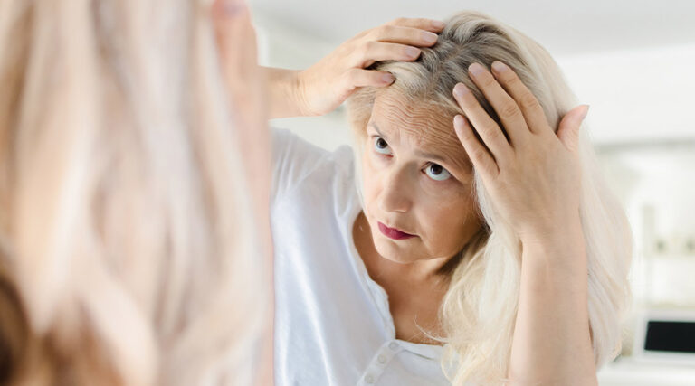 the old lady has her hand placed on her head and is looking at herself in the mirror